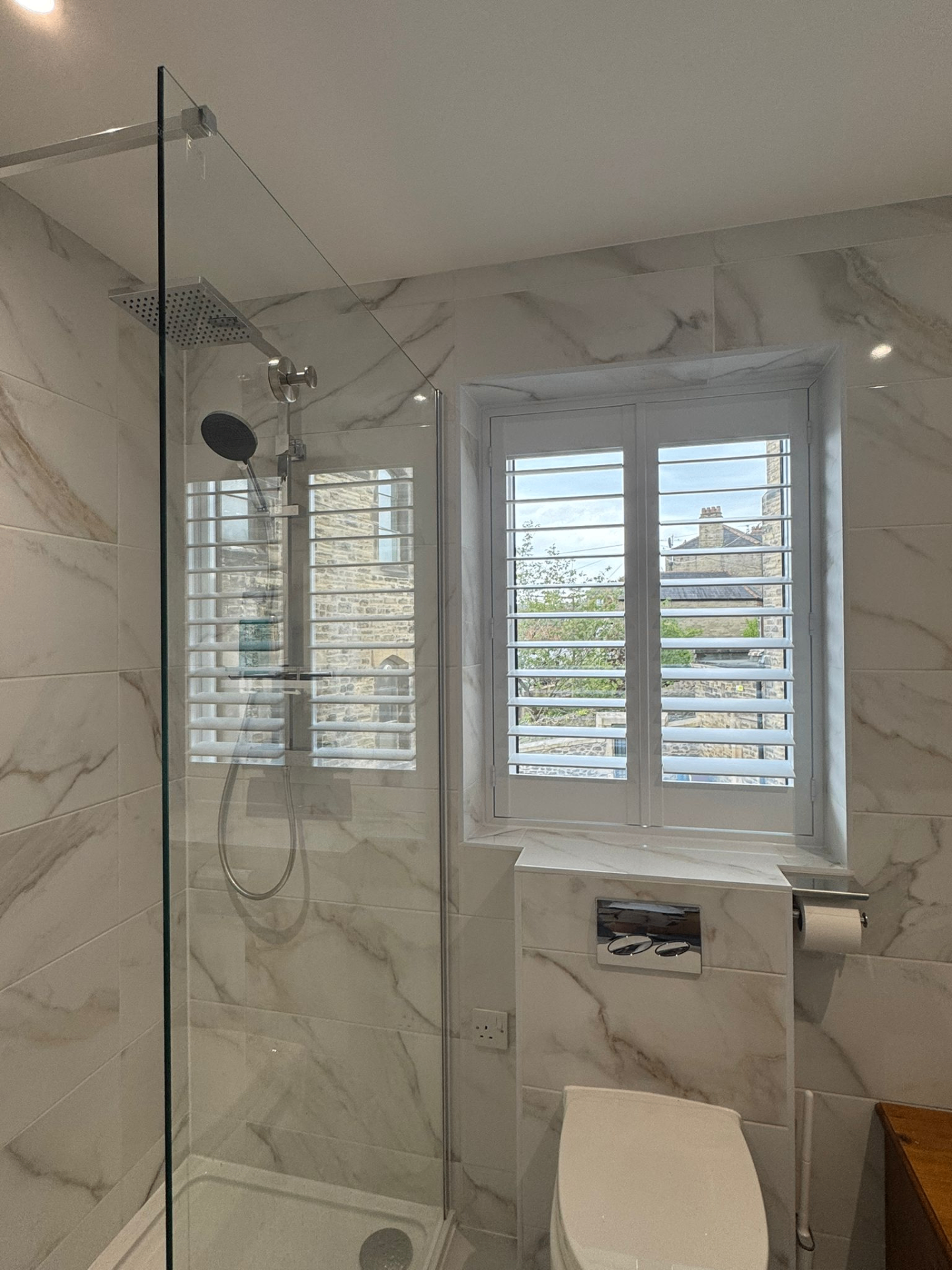 White waterproof PVC shutters fitted to a bathroom window beside a walk-in shower
