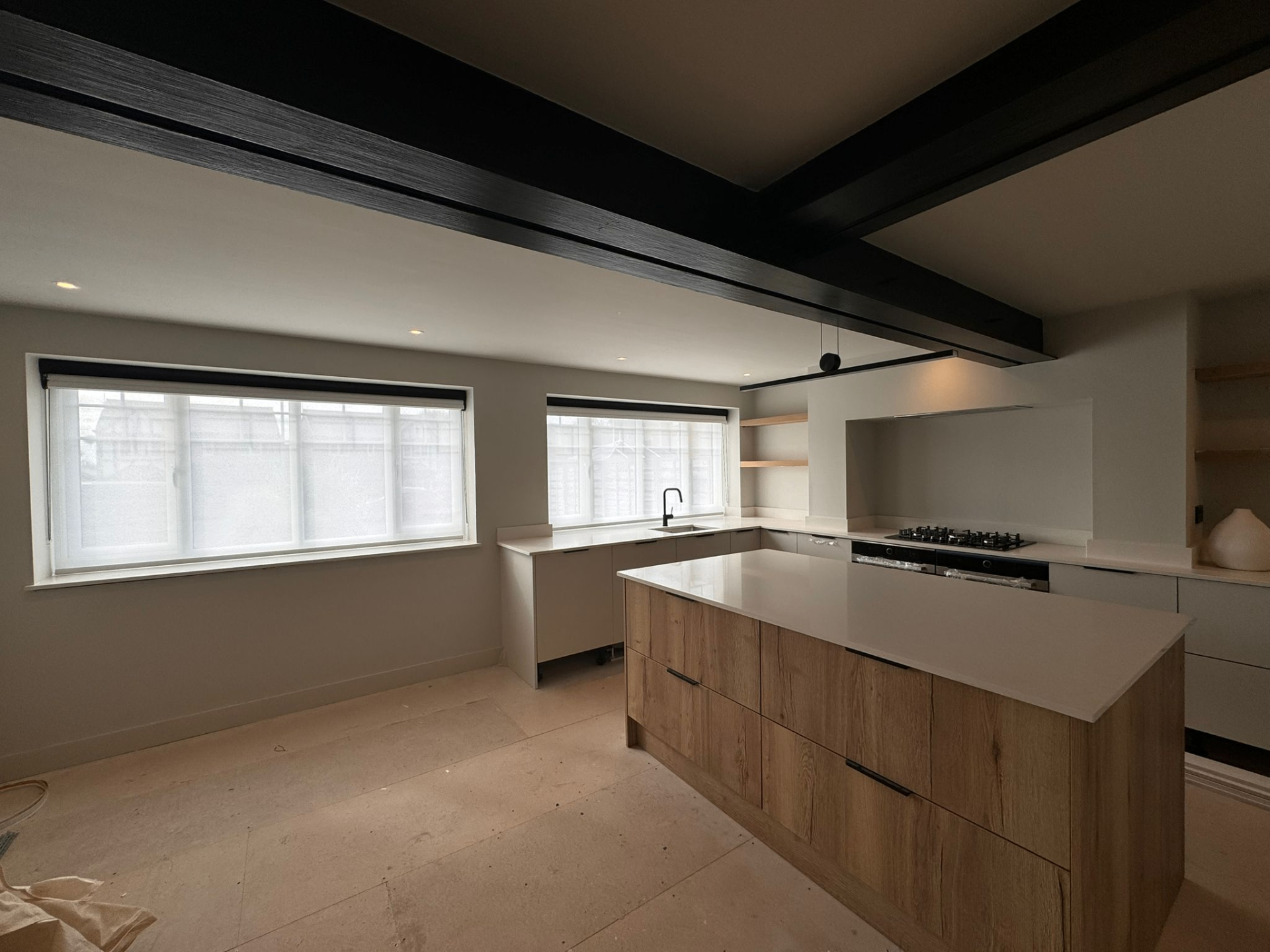 Twin motorised roller blinds fitted in a modern kitchen with dark beams and pale cabinetry