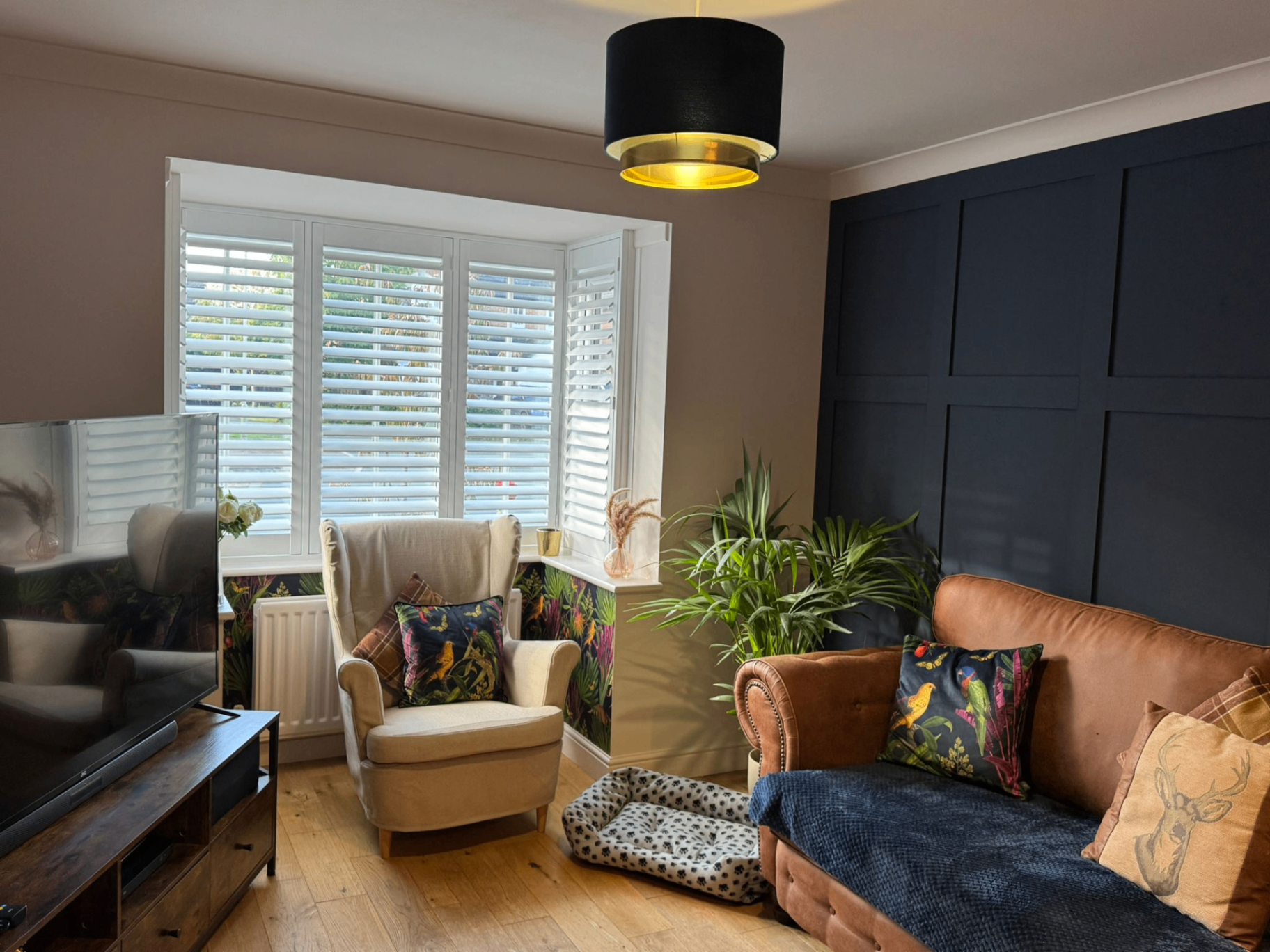 Full height white shutters in a lounge with dark feature wall, leather sofa and bay window
