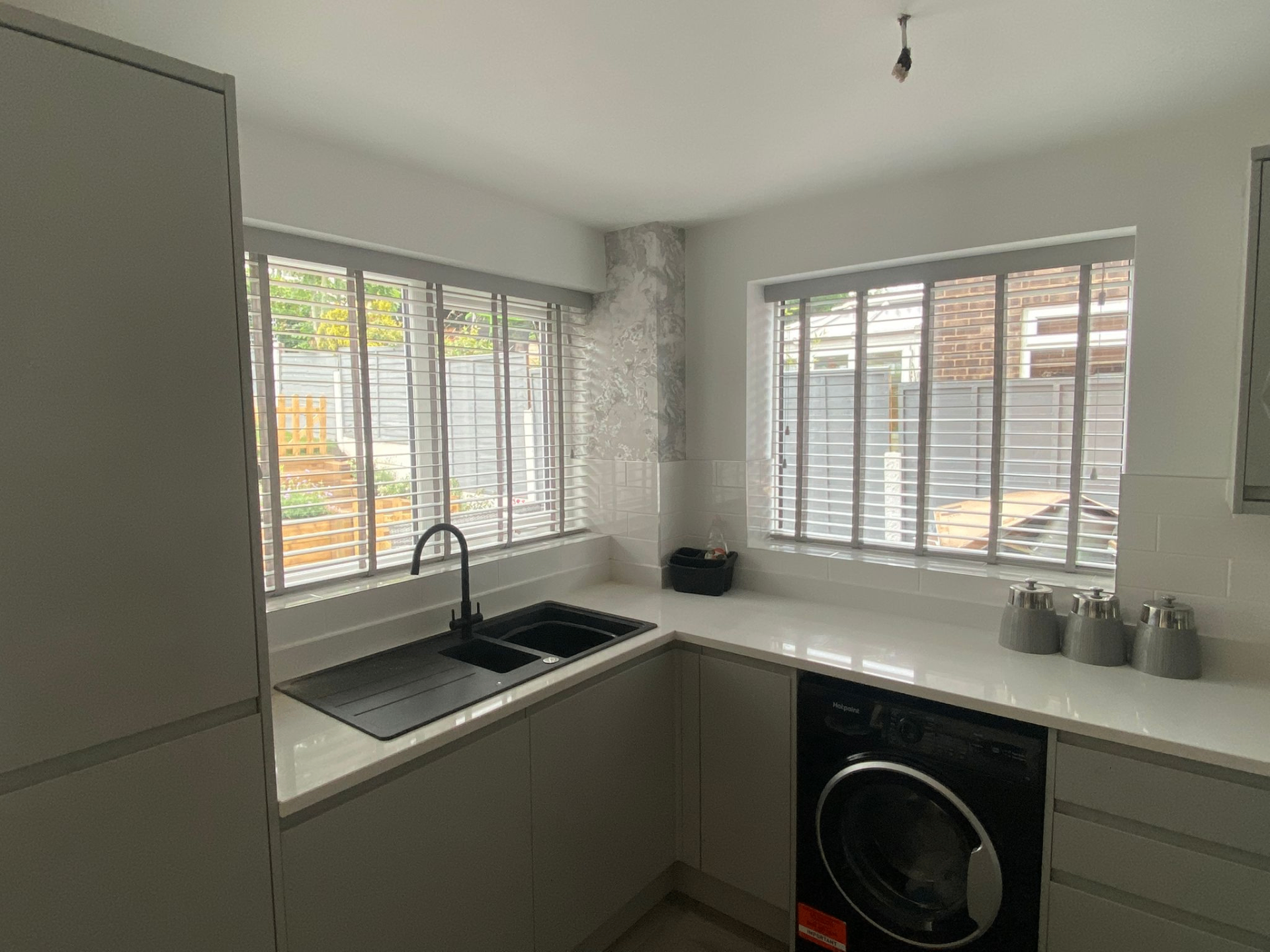 Grey wooden Venetian blinds with matching tapes on two corner kitchen windows