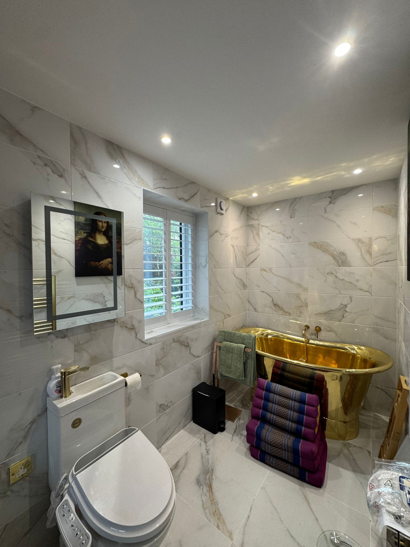 White PVC shutters fitted to a bathroom window beside a gold freestanding bath