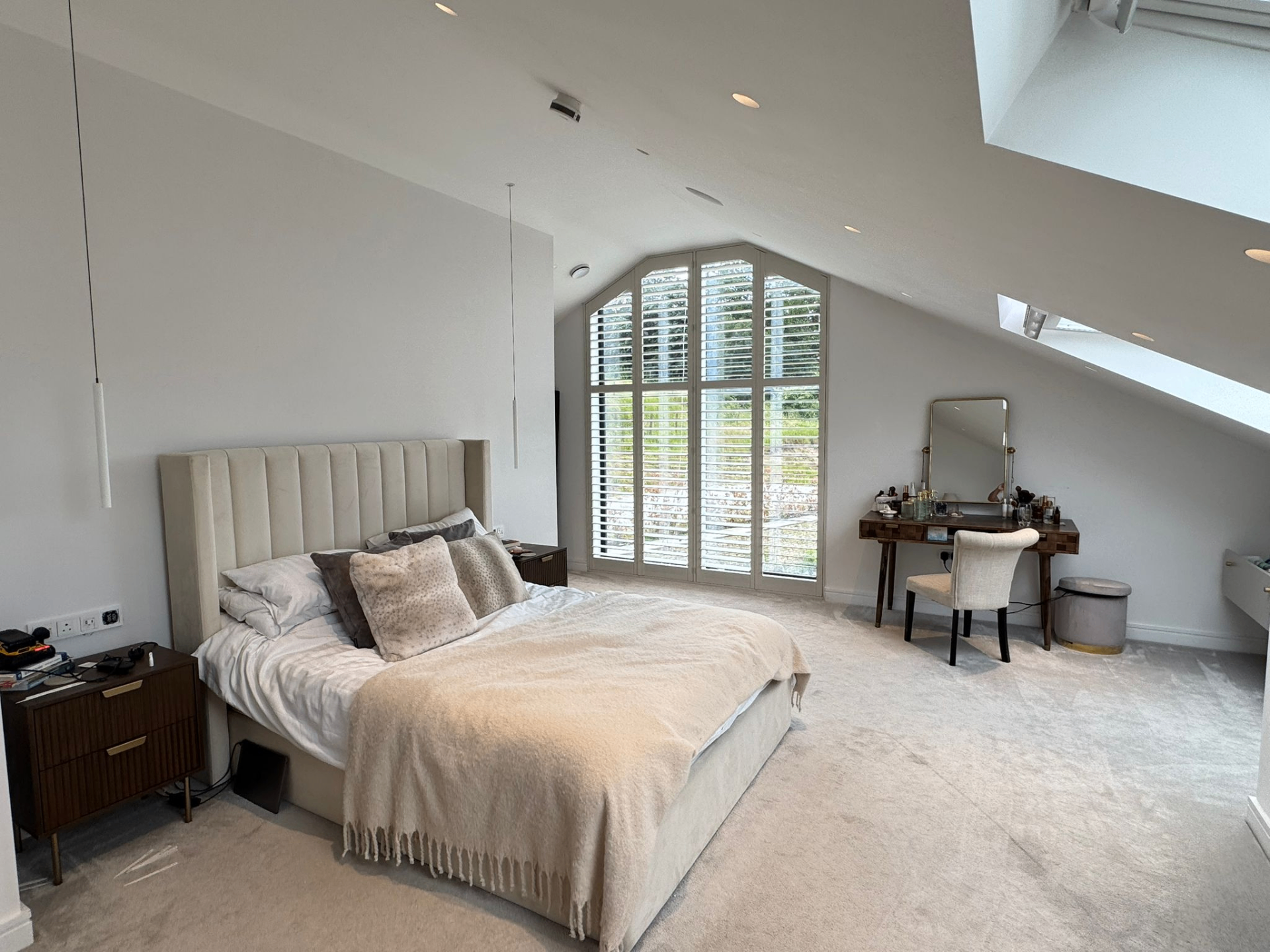 Wide bedroom view showing shaped shutters fitted to a tall gable-end window beneath a pitched loft ceiling