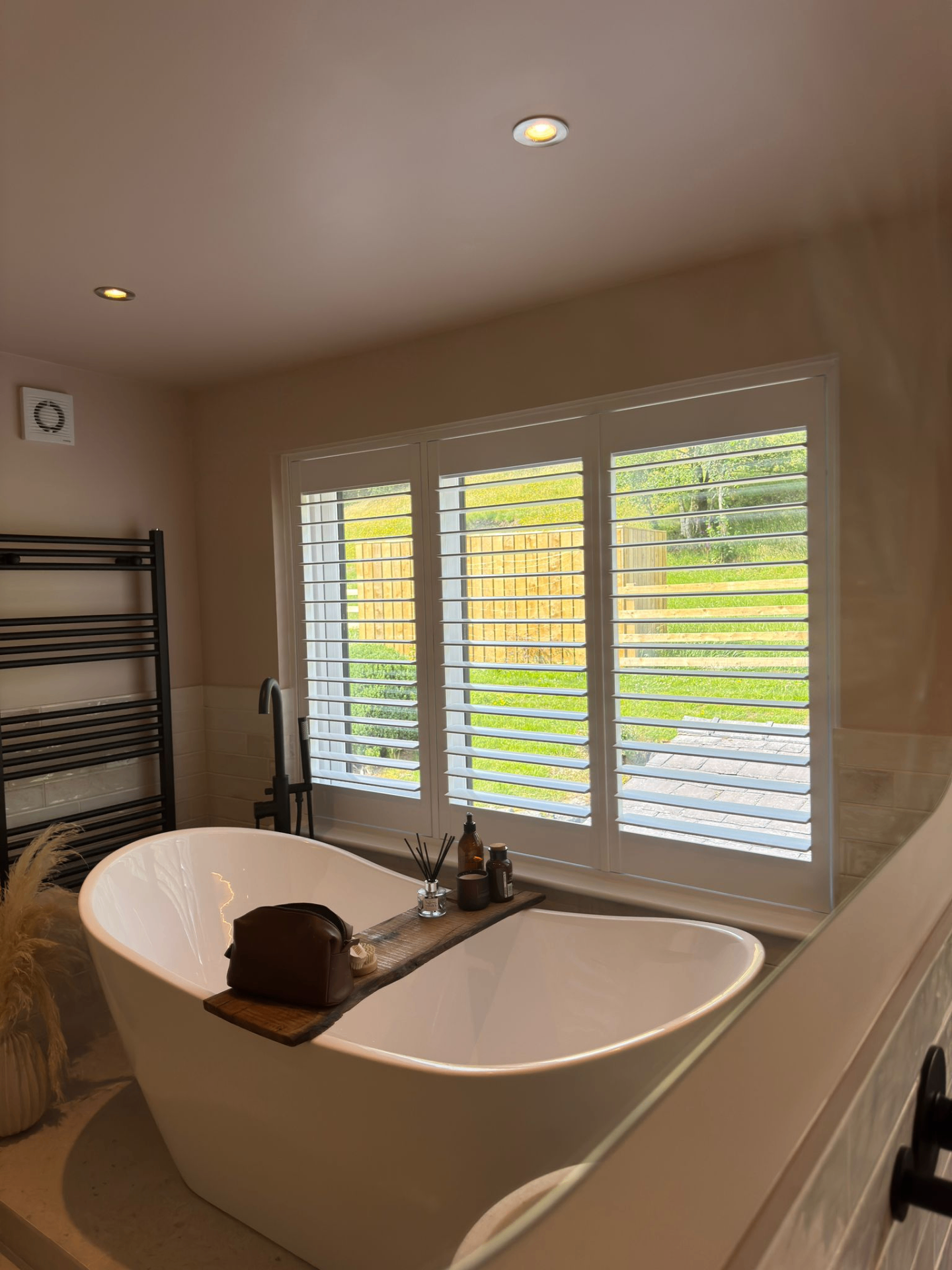 Wide bathroom view with waterproof PVC shutters fitted across a three-panel window above a freestanding bath