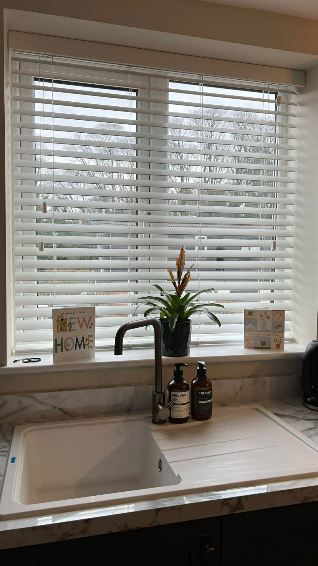 White wooden Venetian blinds in a kitchen above a marble worktop and sink