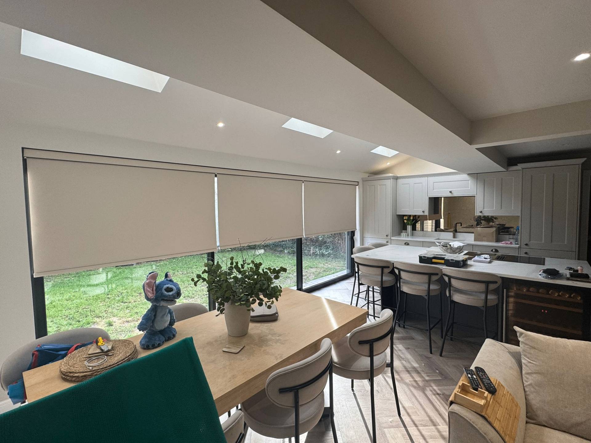 Light motorised roller blinds fitted across wide glazed doors in an open-plan kitchen extension