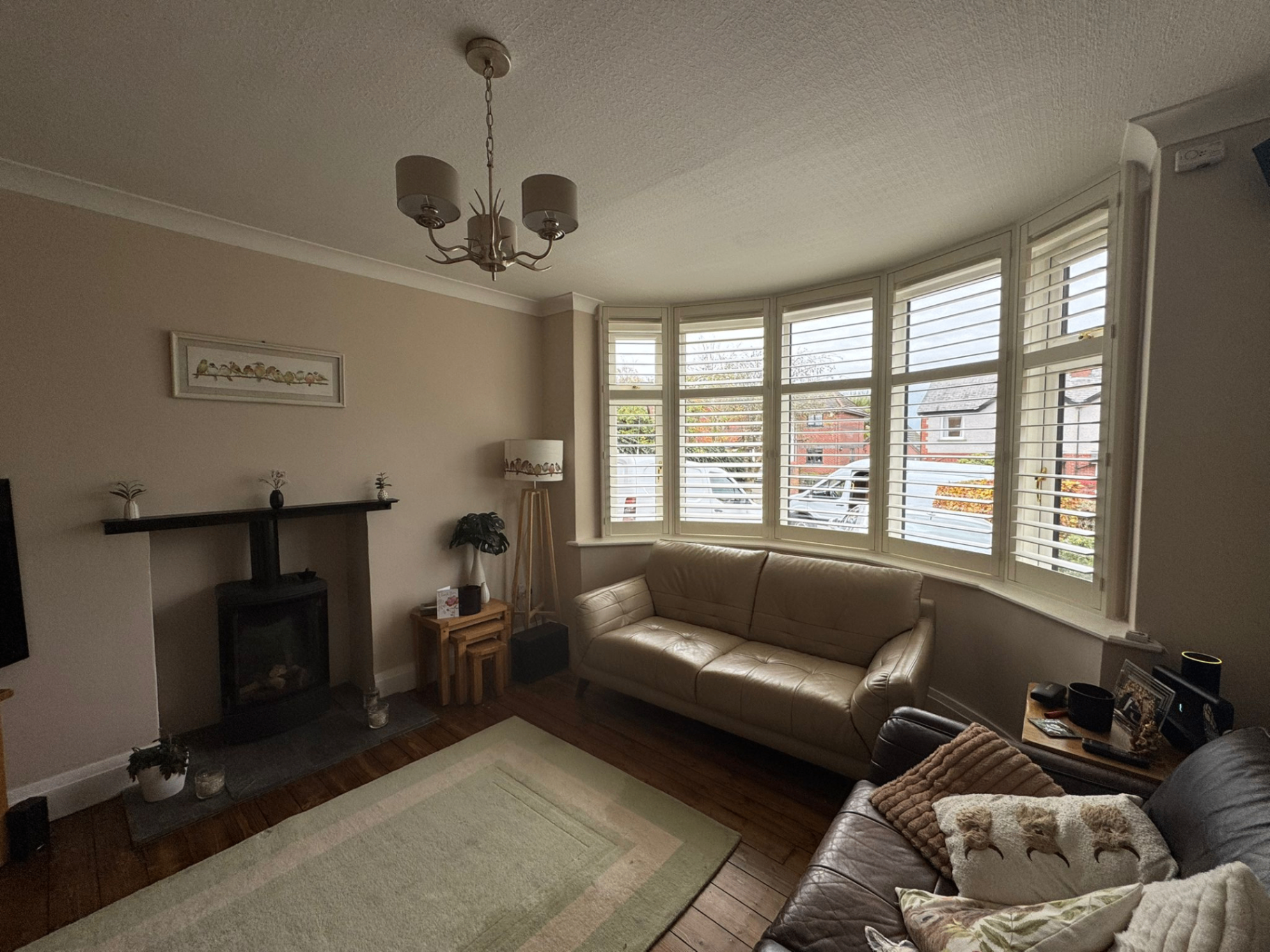 Bay window shutters fitted in a lounge with leather sofas and a wood-burning stove