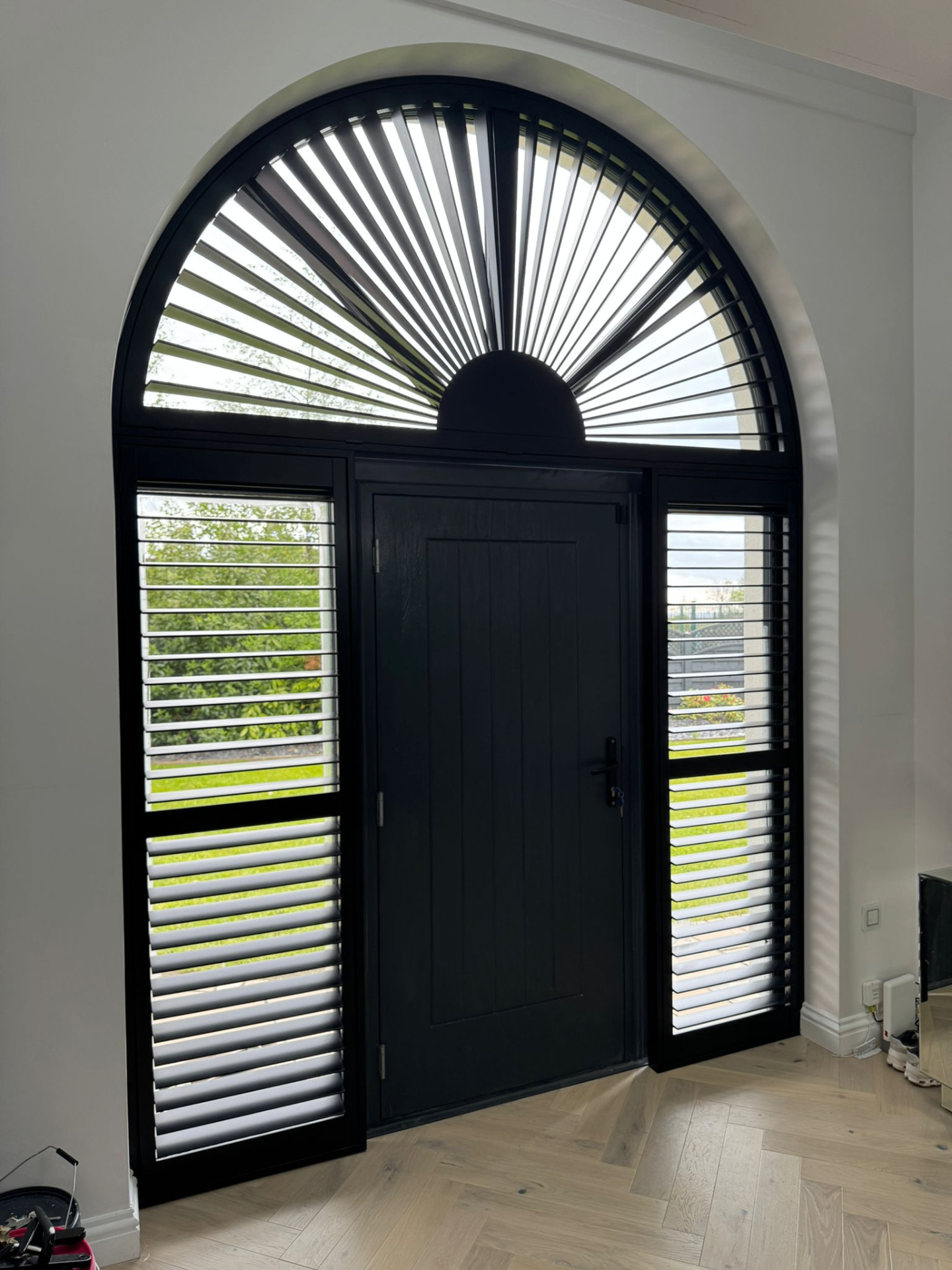 Black shaped shutters fitted around an arched front door with fanlight and side panels