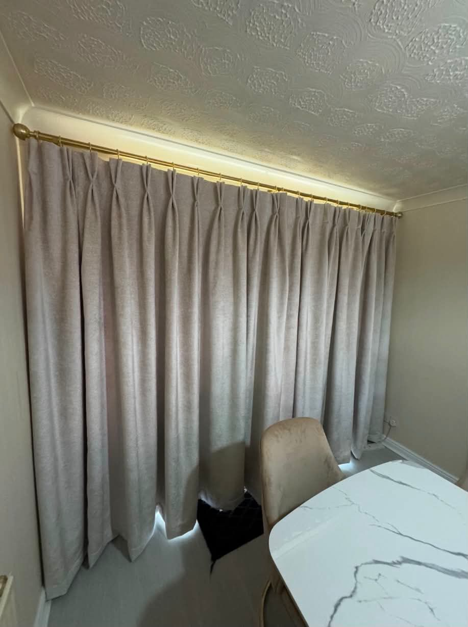Grey pinch pleat curtains on a brass pole in a dining room