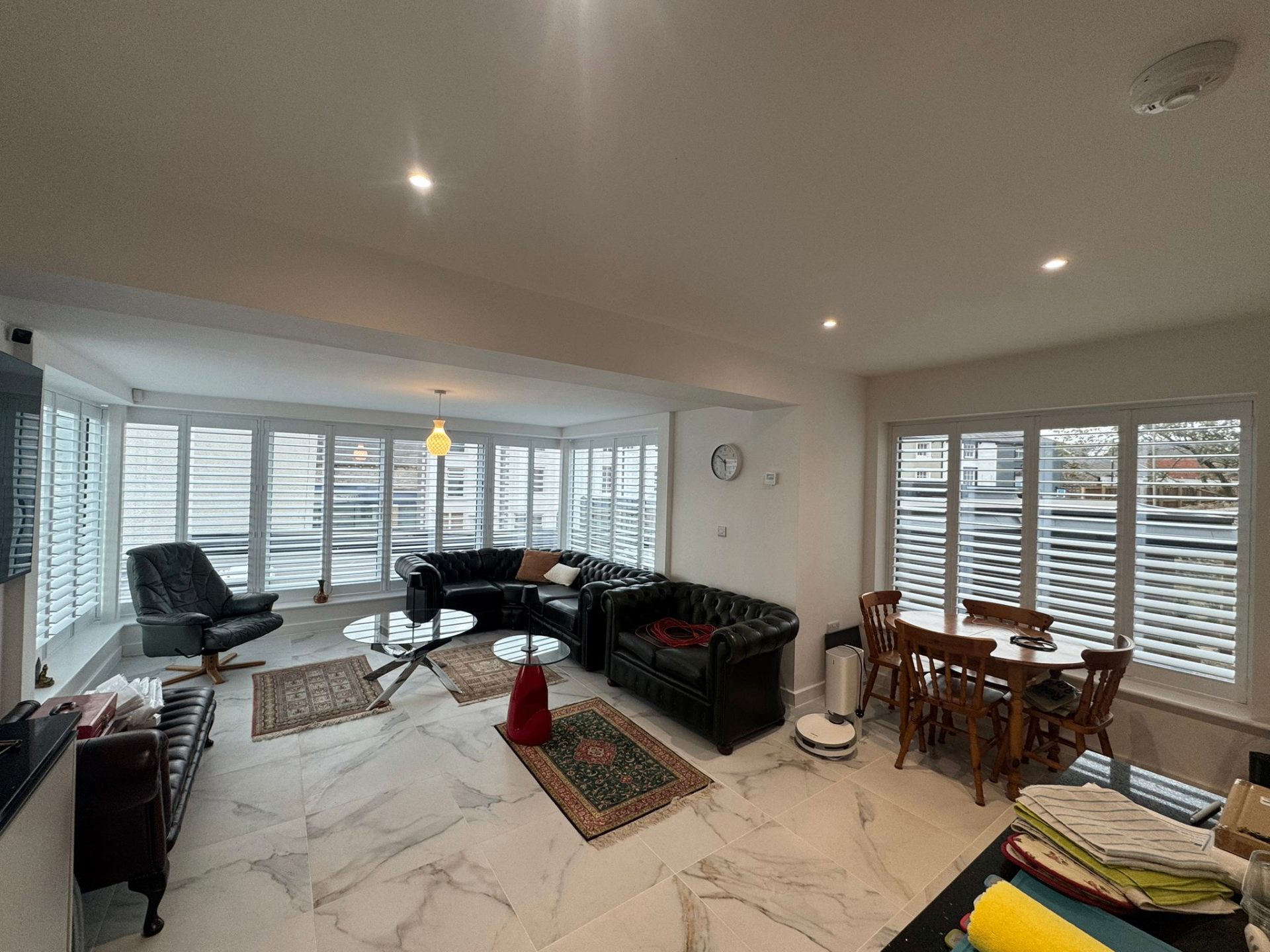 White bifold tracked shutters installed across corner glazing in an open-plan kitchen and seating area