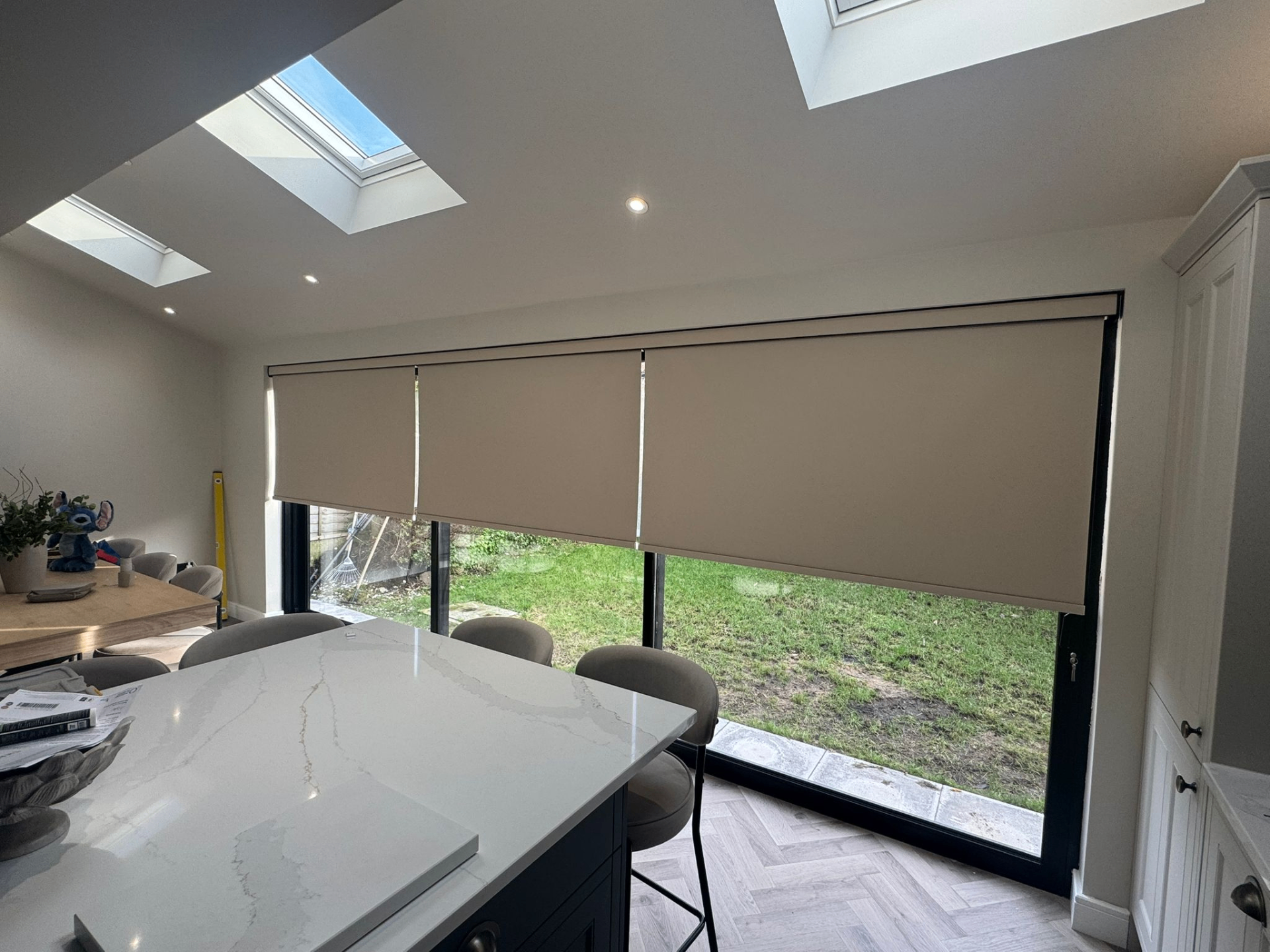 Three motorised roller blinds fitted across a glazed kitchen wall beneath rooflights