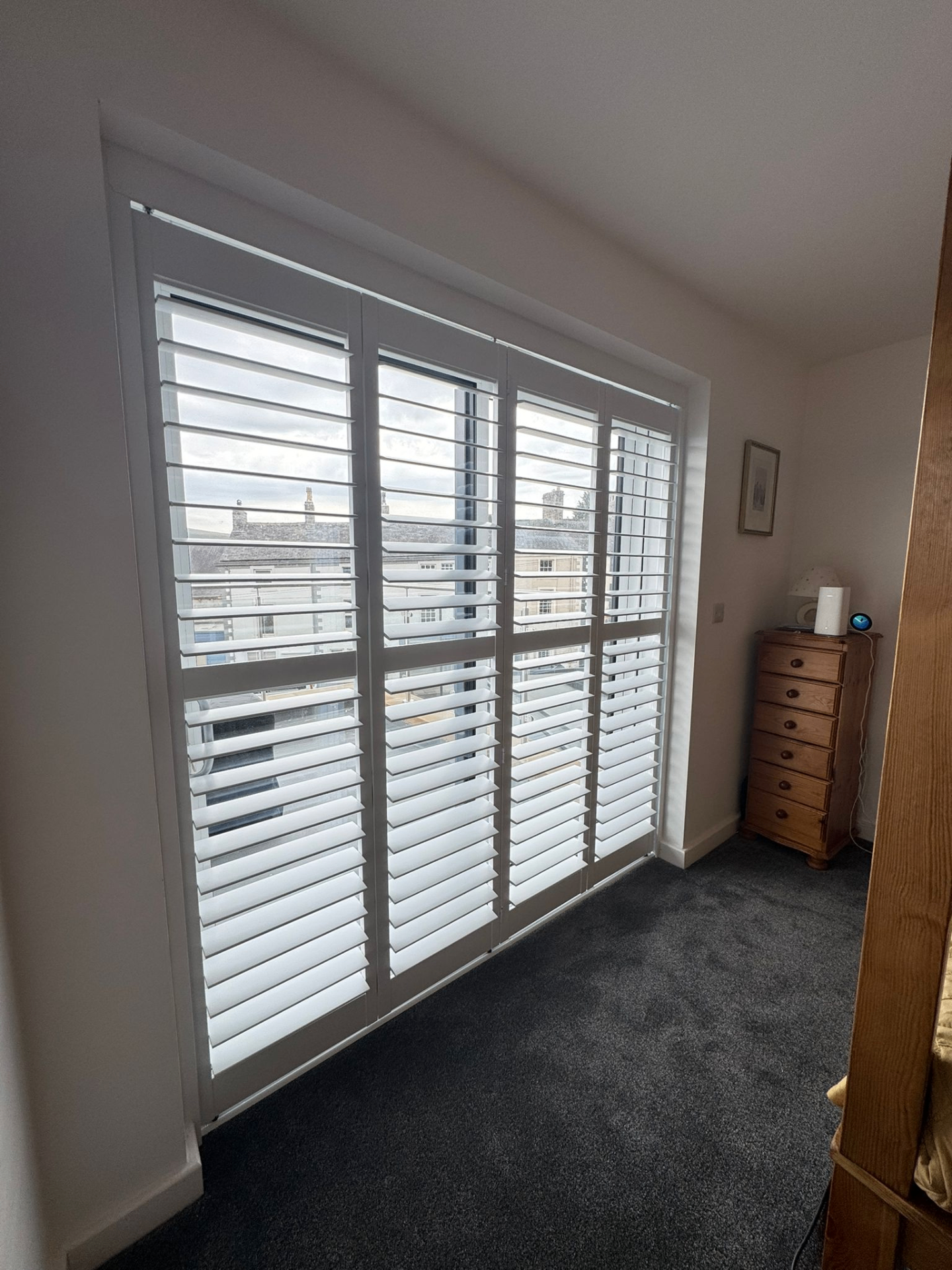 White tracked shutters fitted across a wide bedroom window with four folding panels