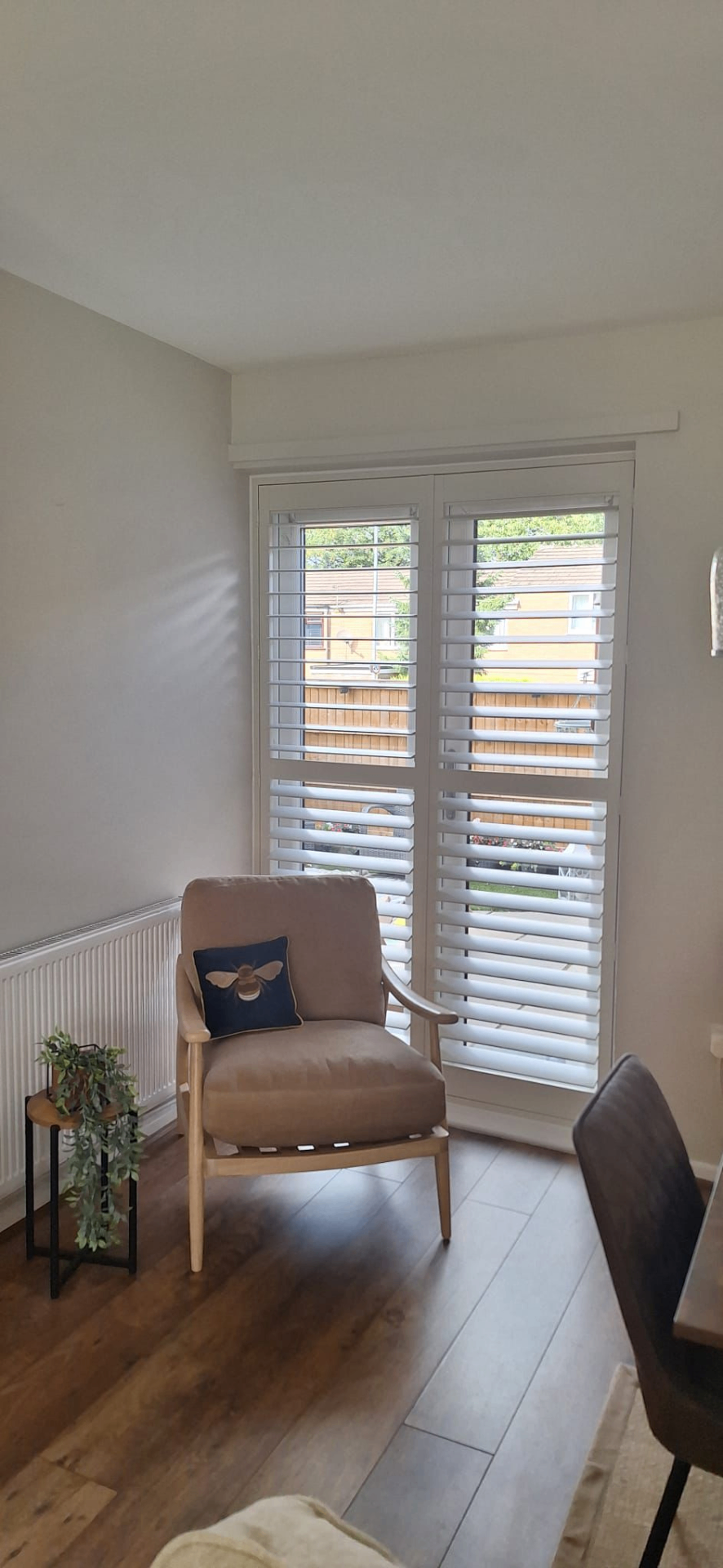 Full height white shutters fitted to glazed doors beside a chair in a dining space