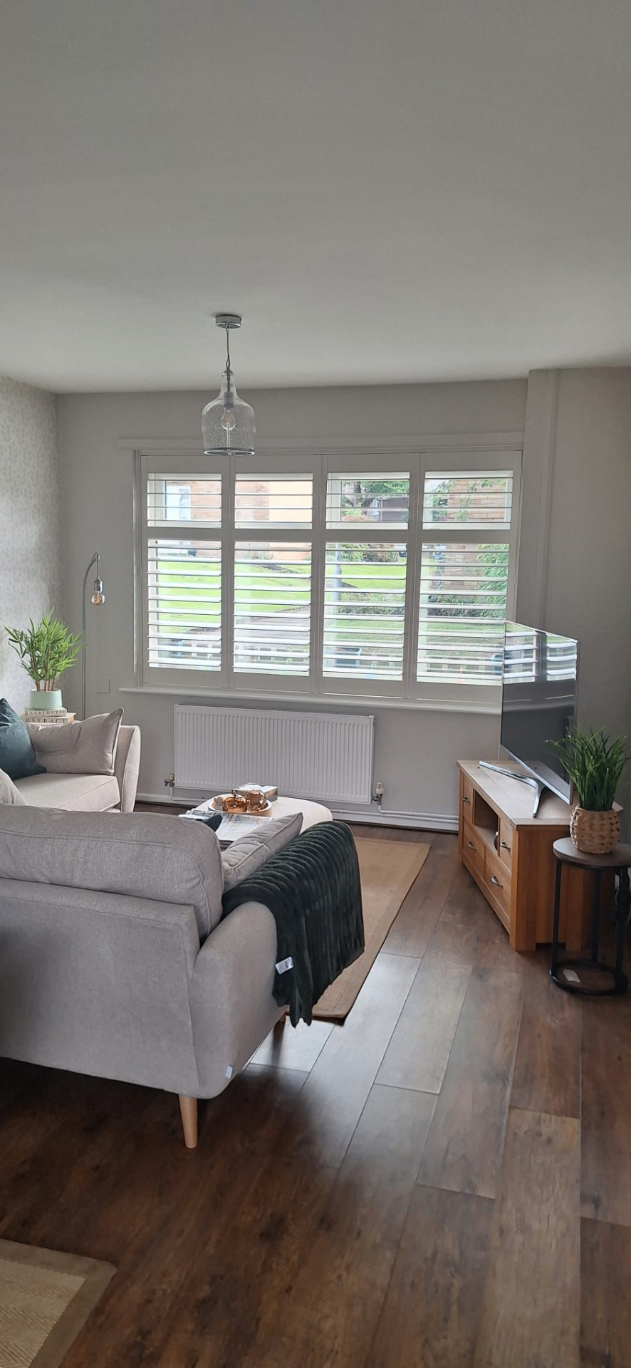 Full height white shutters fitted to a wide living-room window above a radiator
