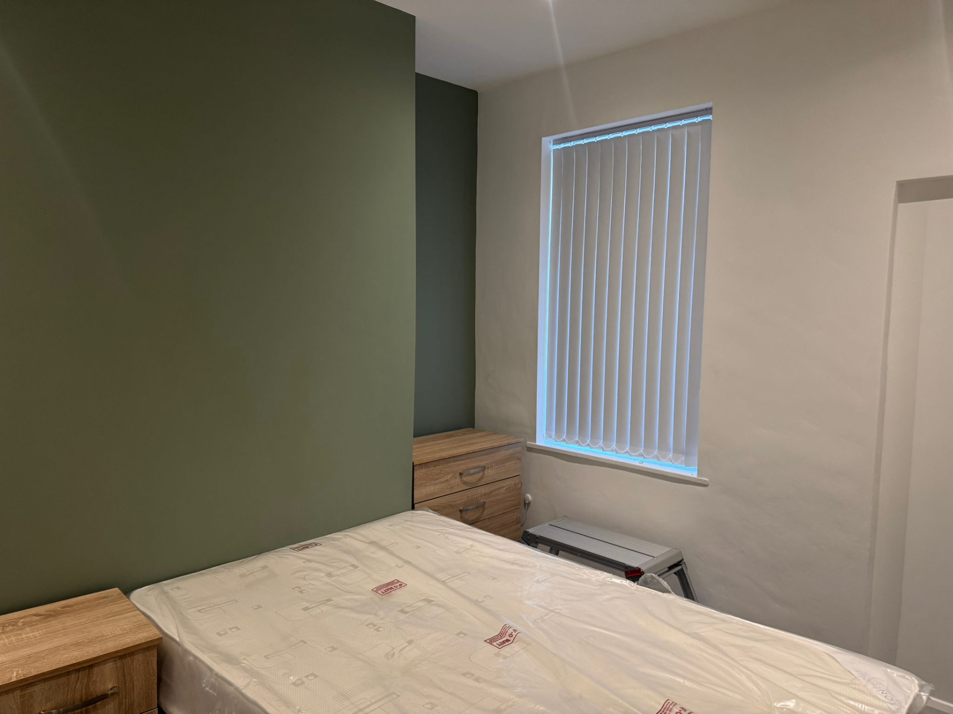 White vertical blinds in a bedroom with sage green feature wall