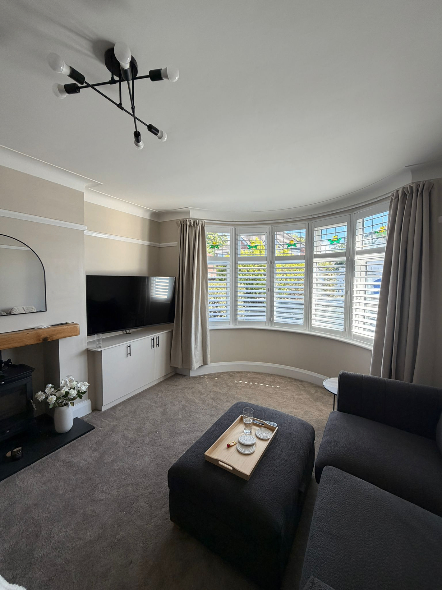 White bay window shutters fitted in a curved living room with media unit and dark seating
