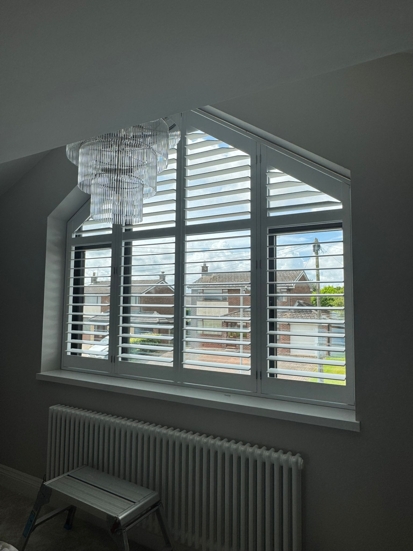 White shaped shutters fitted to a gable window with angled top sections in a loft room